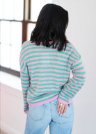 Person wearing a pink and green striped sweater with light blue jeans indoors.