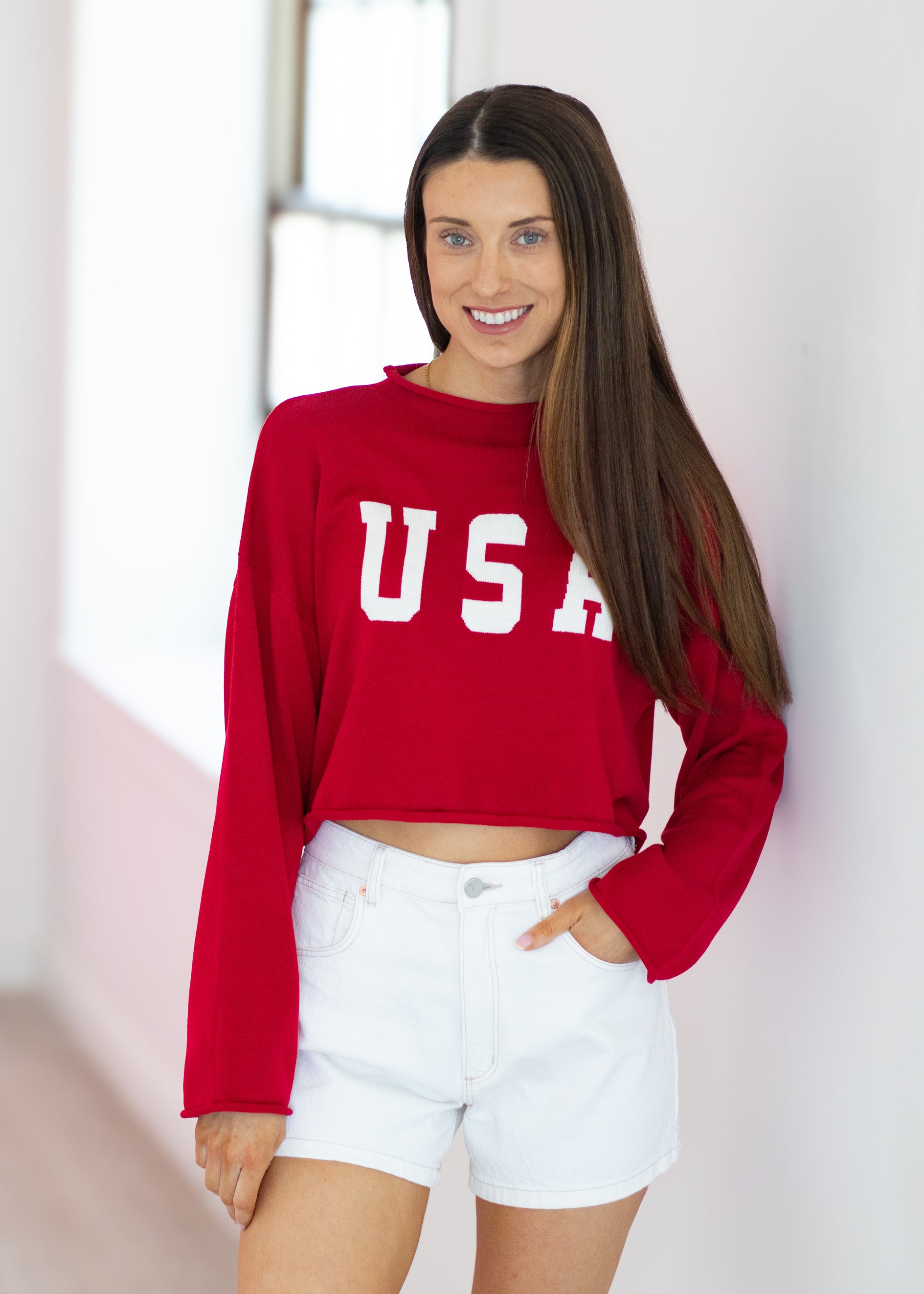 Woman wearing a red 'USA' sweatshirt and white shorts indoors.