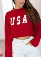 Person wearing a red 'USA' crop top with white pants against a neutral background