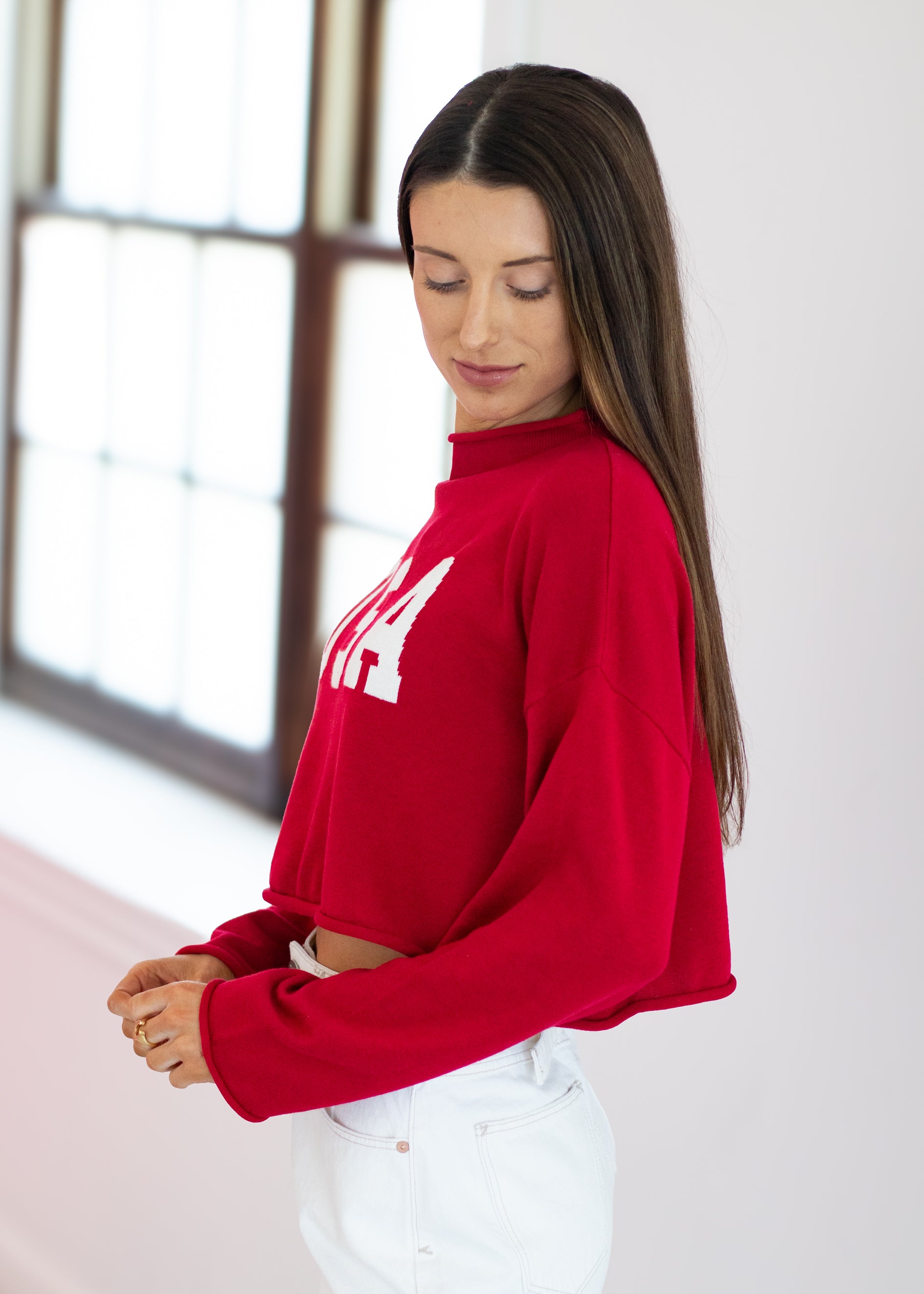 Woman wearing a red sweatshirt with a white logo in a bright room.