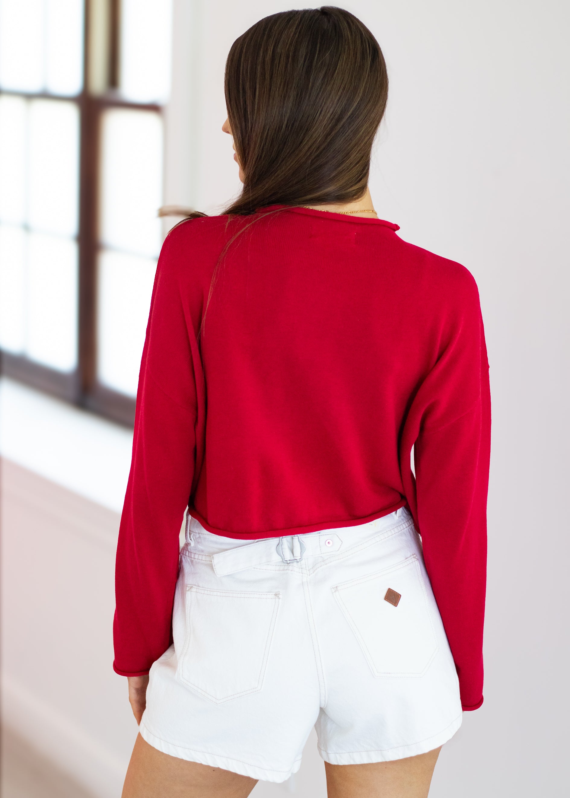 Person wearing a red sweater and white shorts in a minimal indoor setting