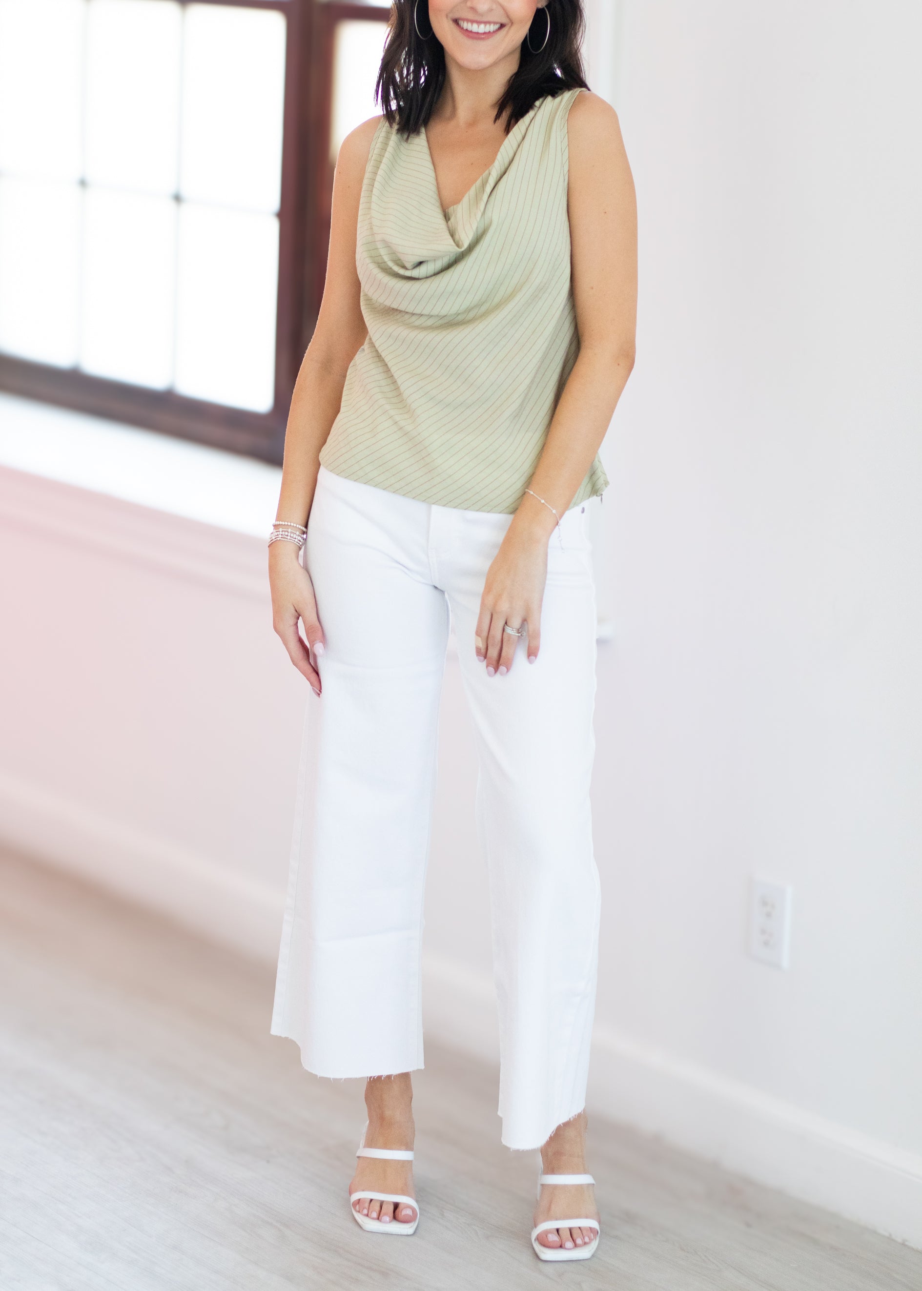 Woman wearing a green sleeveless top and white pants in a bright room.