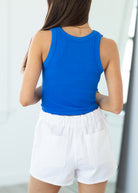 Person wearing a blue tank top and white shorts against a light background