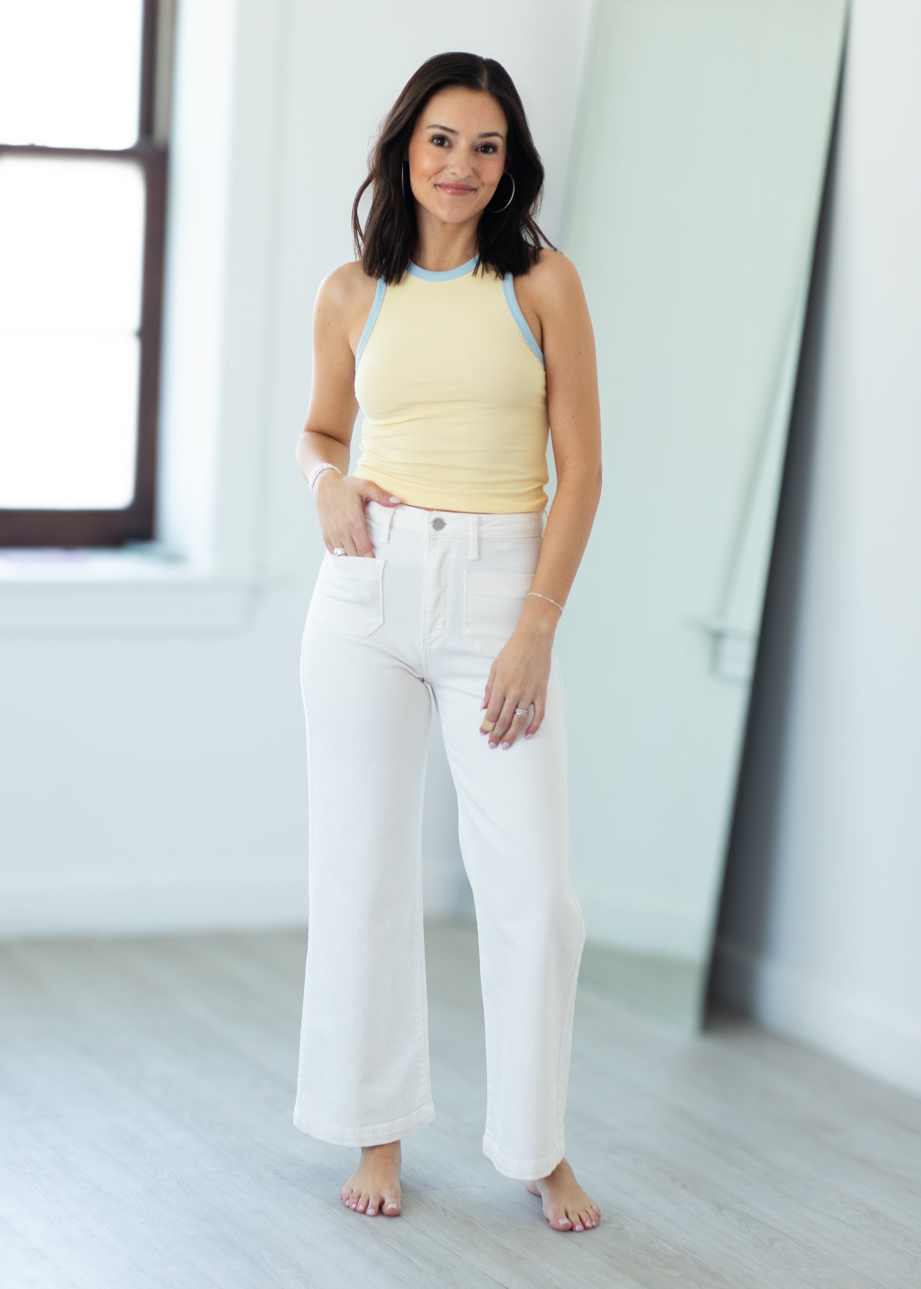 Woman wearing a yellow top and white pants in a minimalistic room.