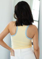 Woman wearing a yellow tank top with light blue trim, standing against a neutral background.