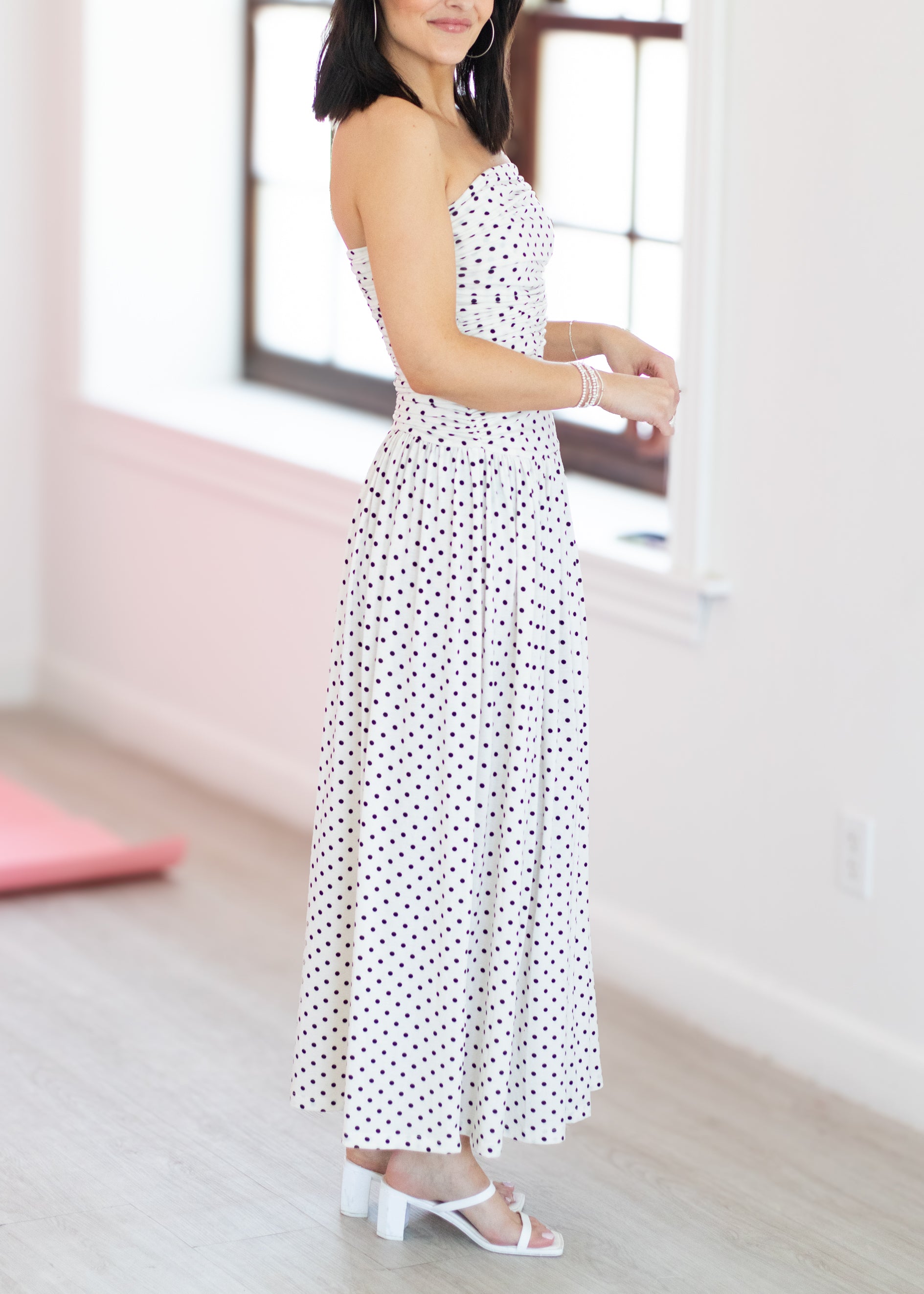 Woman wearing a white dress with black polka dots in an indoor setting.
