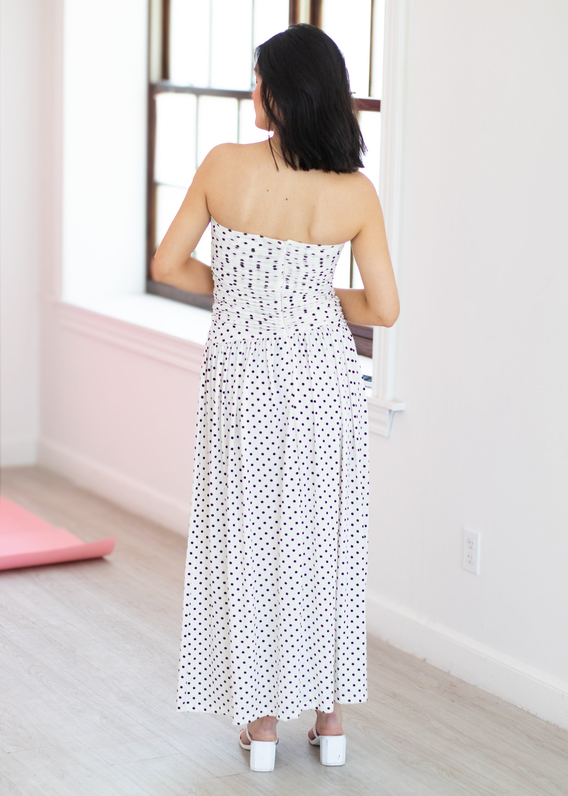 Woman wearing a white strapless dress with black polka dots in a room.