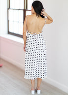 Woman wearing a polka dot dress with a backless design, standing in a room with a window.