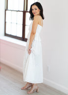 Woman wearing a white dress in a bright room with large windows.