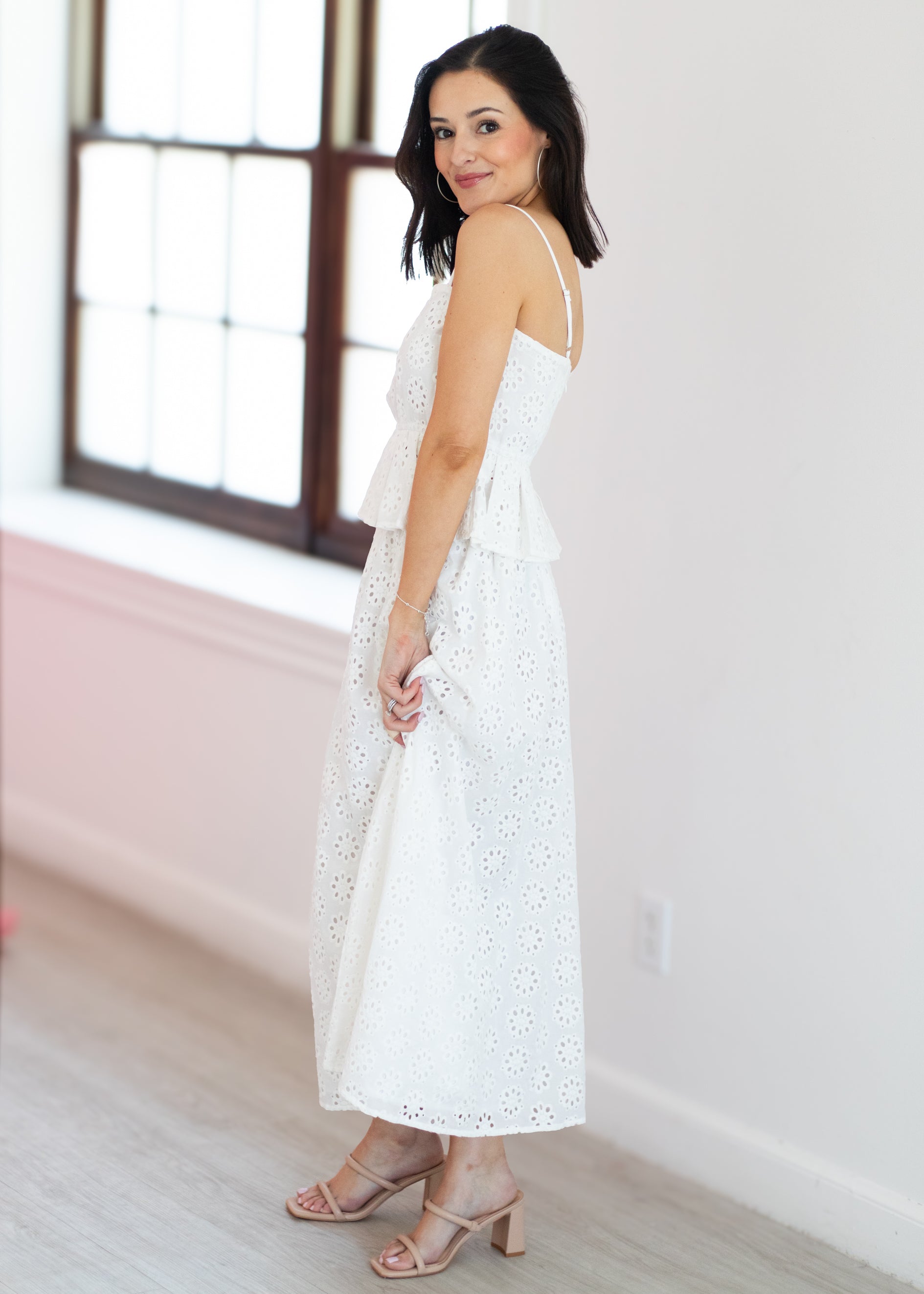 Woman wearing a white dress in a bright room with large windows.