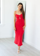 Woman wearing a red dress standing against a white wall.