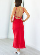 Woman wearing a red dress with thin straps and open back, standing against a white wall.