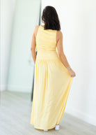 Woman wearing a yellow dress standing against a white wall.