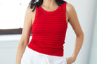 Woman wearing a red sleeveless top and white shorts indoors.