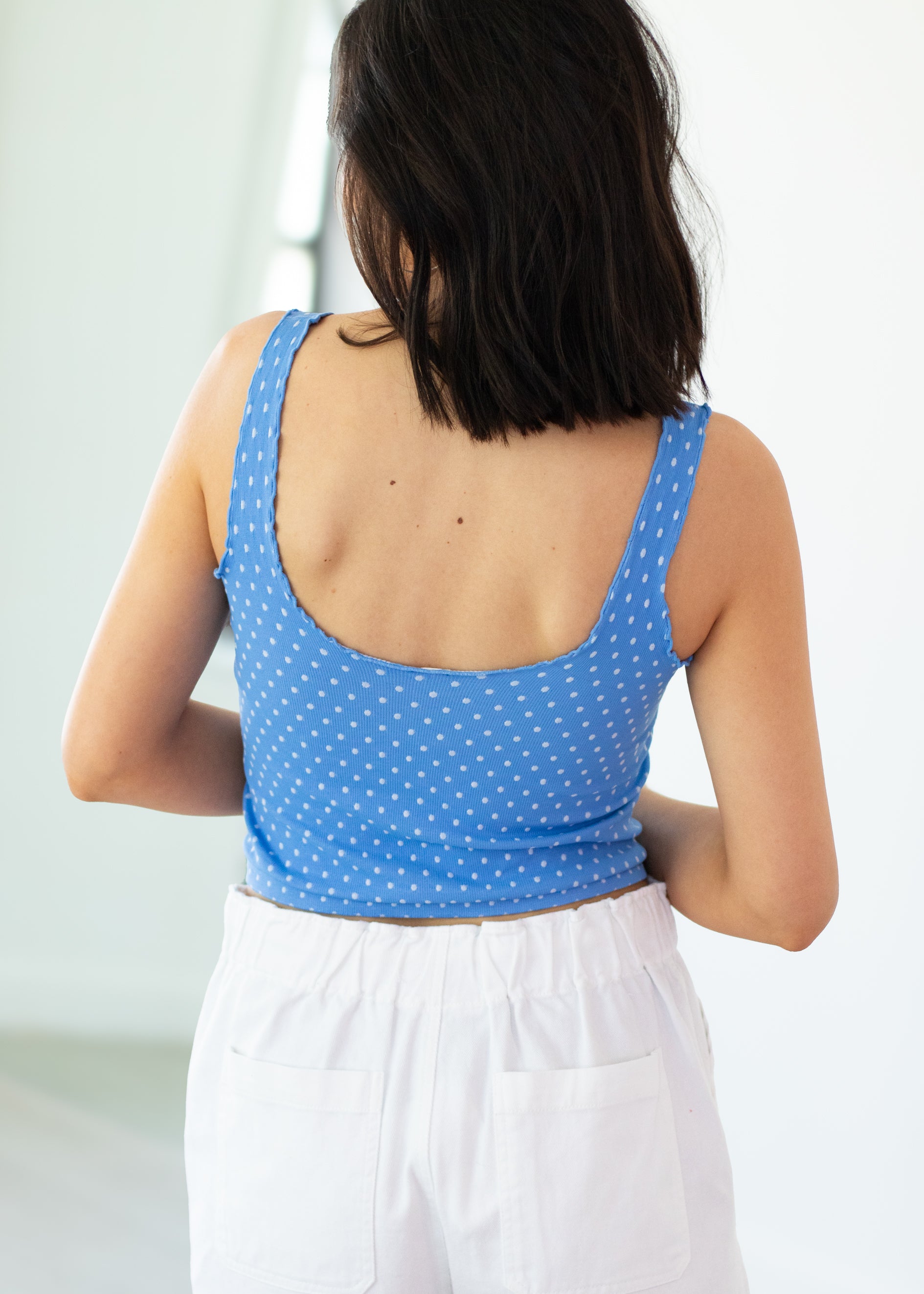 Person wearing a blue polka dot tank top and white pants against a light background
