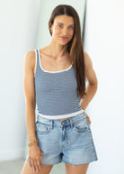 Woman wearing a striped tank top and denim shorts against a light background