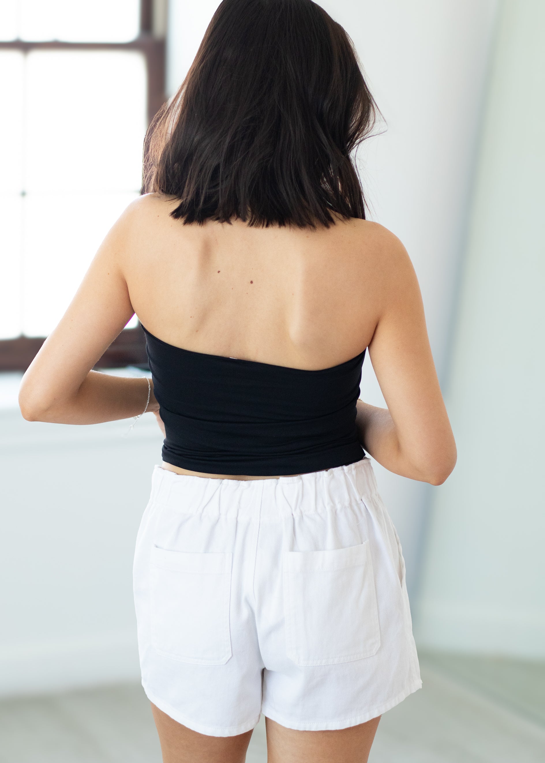 Person wearing a black tube top and white shorts in a minimal indoor setting