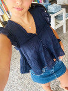 Woman wearing a navy blue top and denim shorts in an outdoor setting.