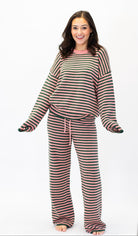 A woman modeling a matching two-piece lounge set with horizontal stripes in pink, and dark green, featuring a long-sleeve top and wide-leg pants, against a plain white background.
