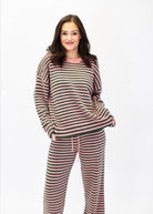A woman modeling a matching two-piece loungewear set featuring a long-sleeve knit top and sweatpants with horizontal stripes in pink, dark green, and cream, set against a plain white background.