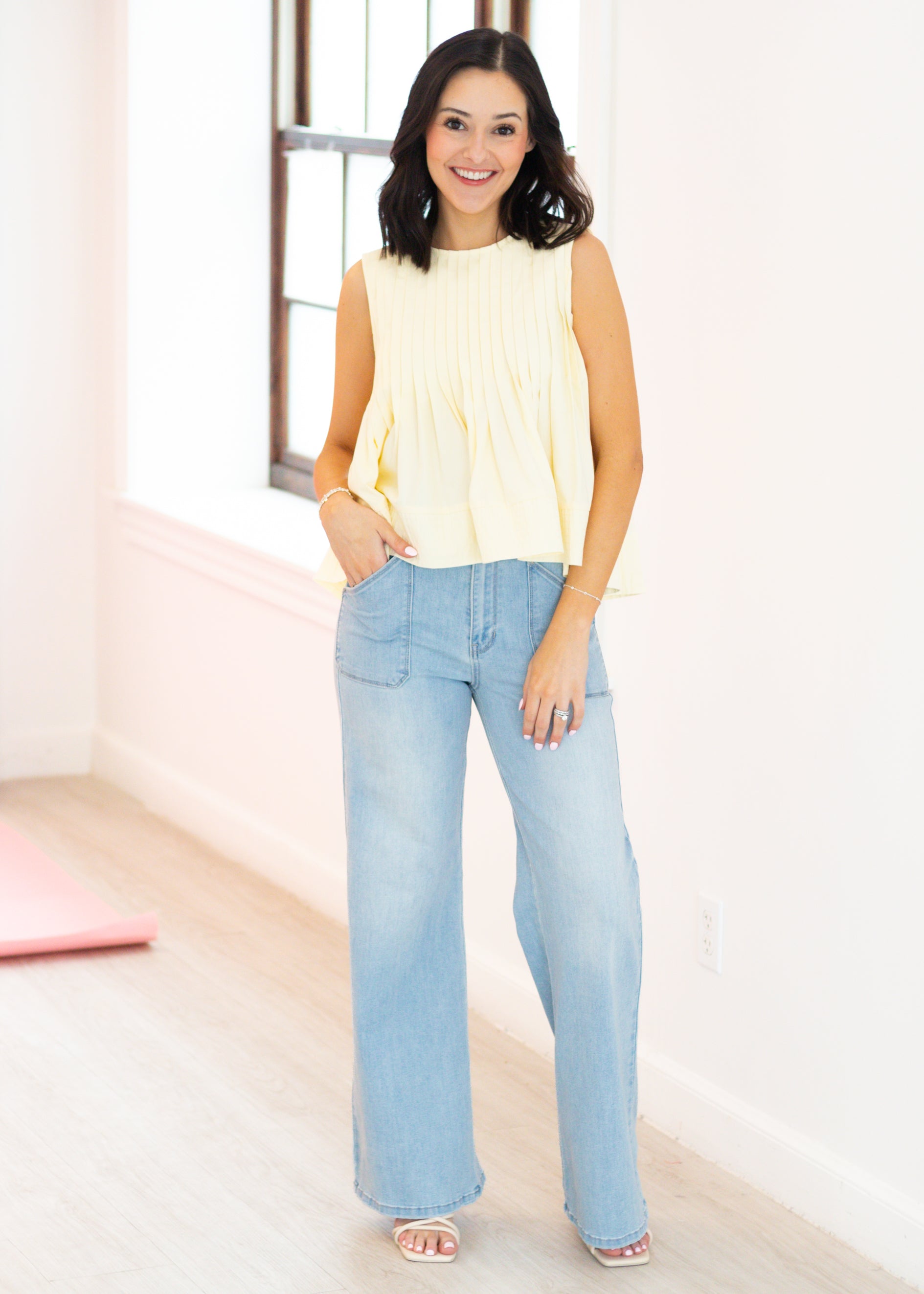 Woman wearing a yellow sleeveless top and light blue jeans indoors.