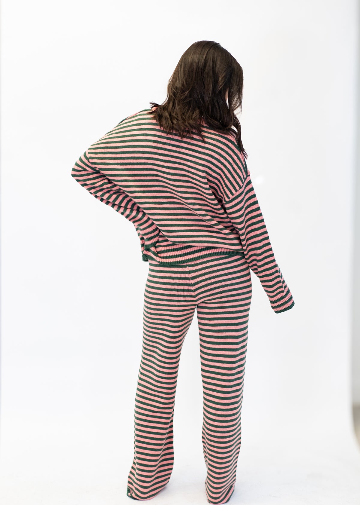 A woman shown from behind wearing a matching two-piece loungewear set with horizontal stripes in beige, red, and dark green, against a plain white studio background.
