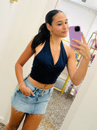 Woman taking a mirror selfie wearing a navy top and denim skirt.