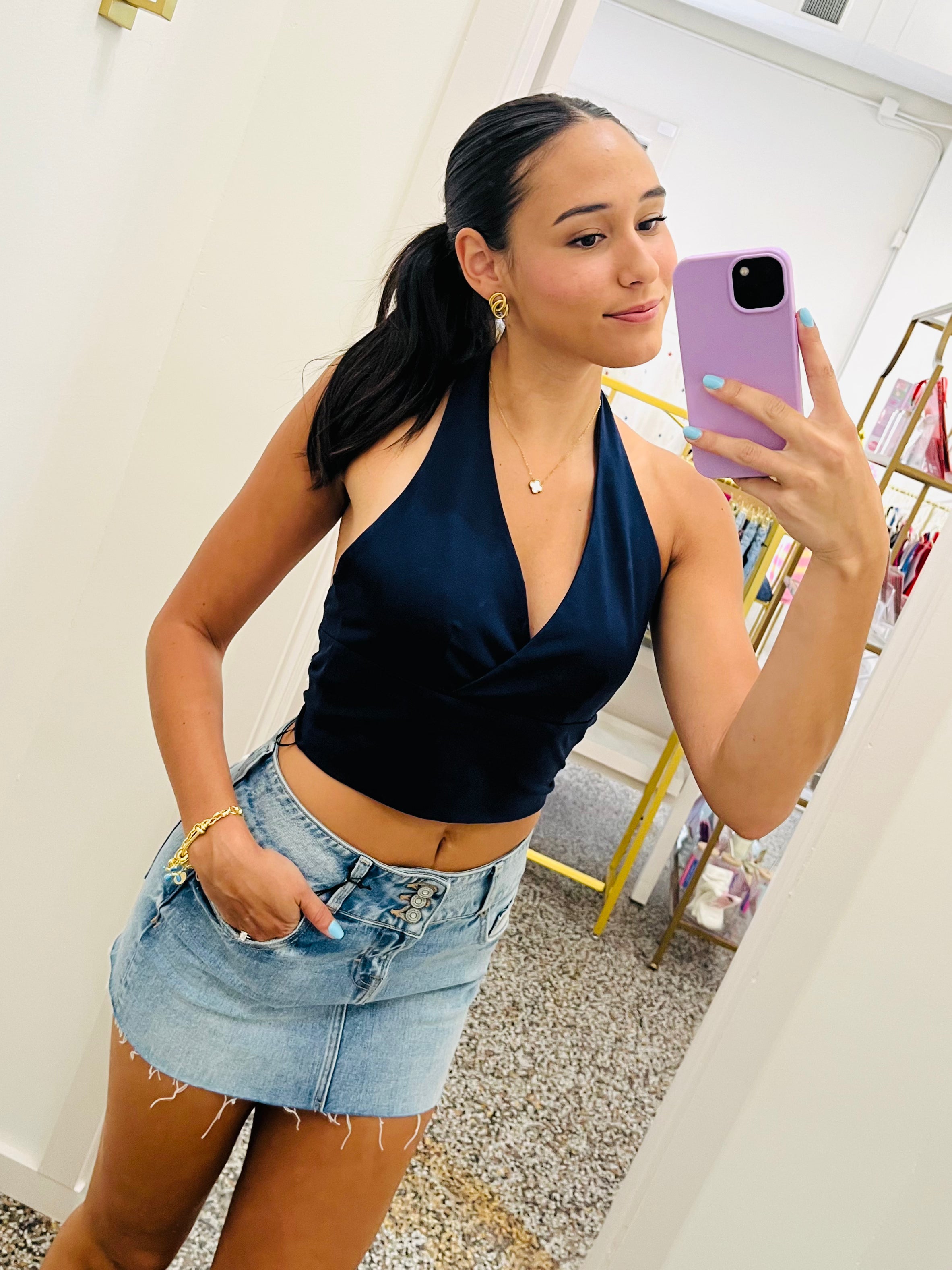 Woman taking a mirror selfie wearing a navy top and denim skirt.