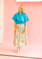 Woman wearing a blue shirt and floral skirt against a pink background