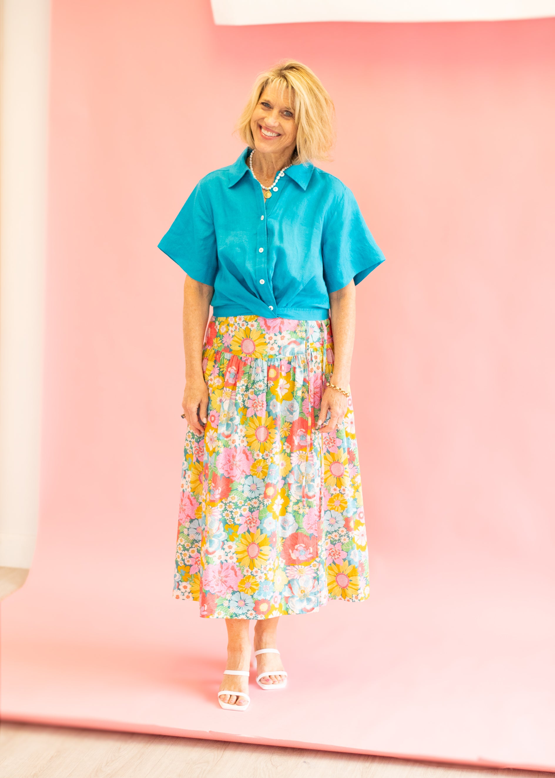 Woman wearing a blue shirt and floral skirt against a pink background