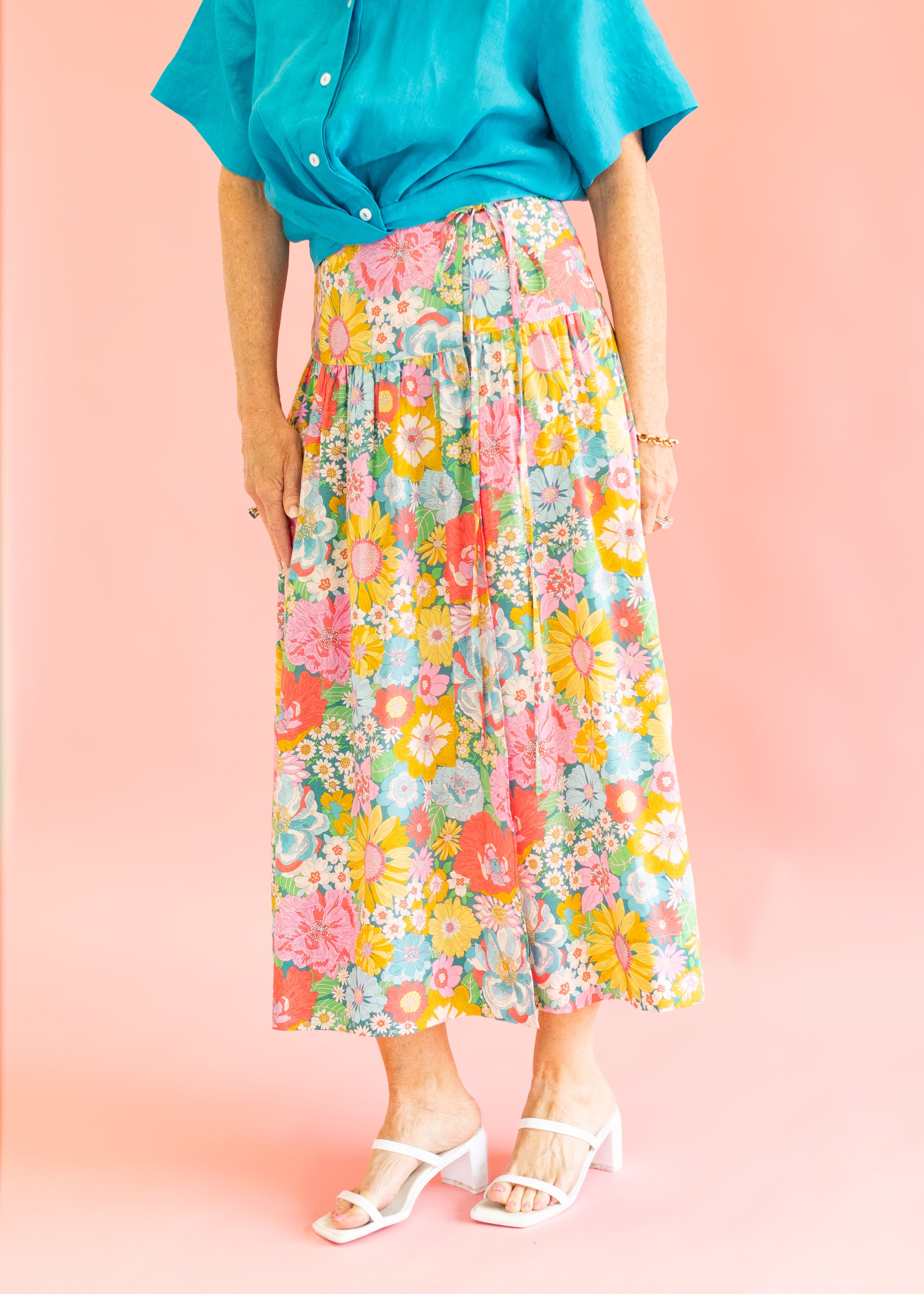 Person wearing a colorful floral skirt and turquoise top on a pink background