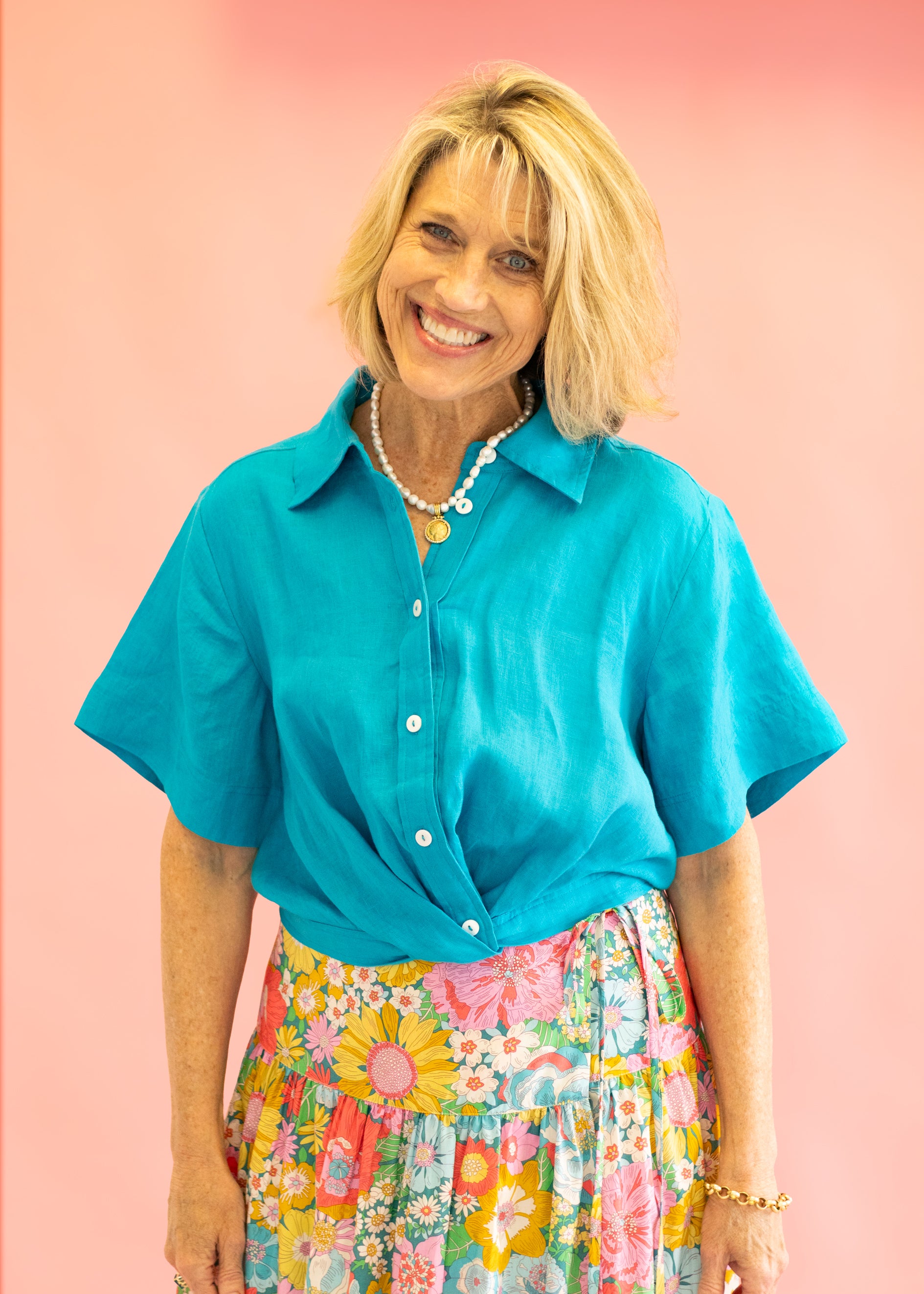 Woman wearing a turquoise shirt and colorful floral skirt against a pink background