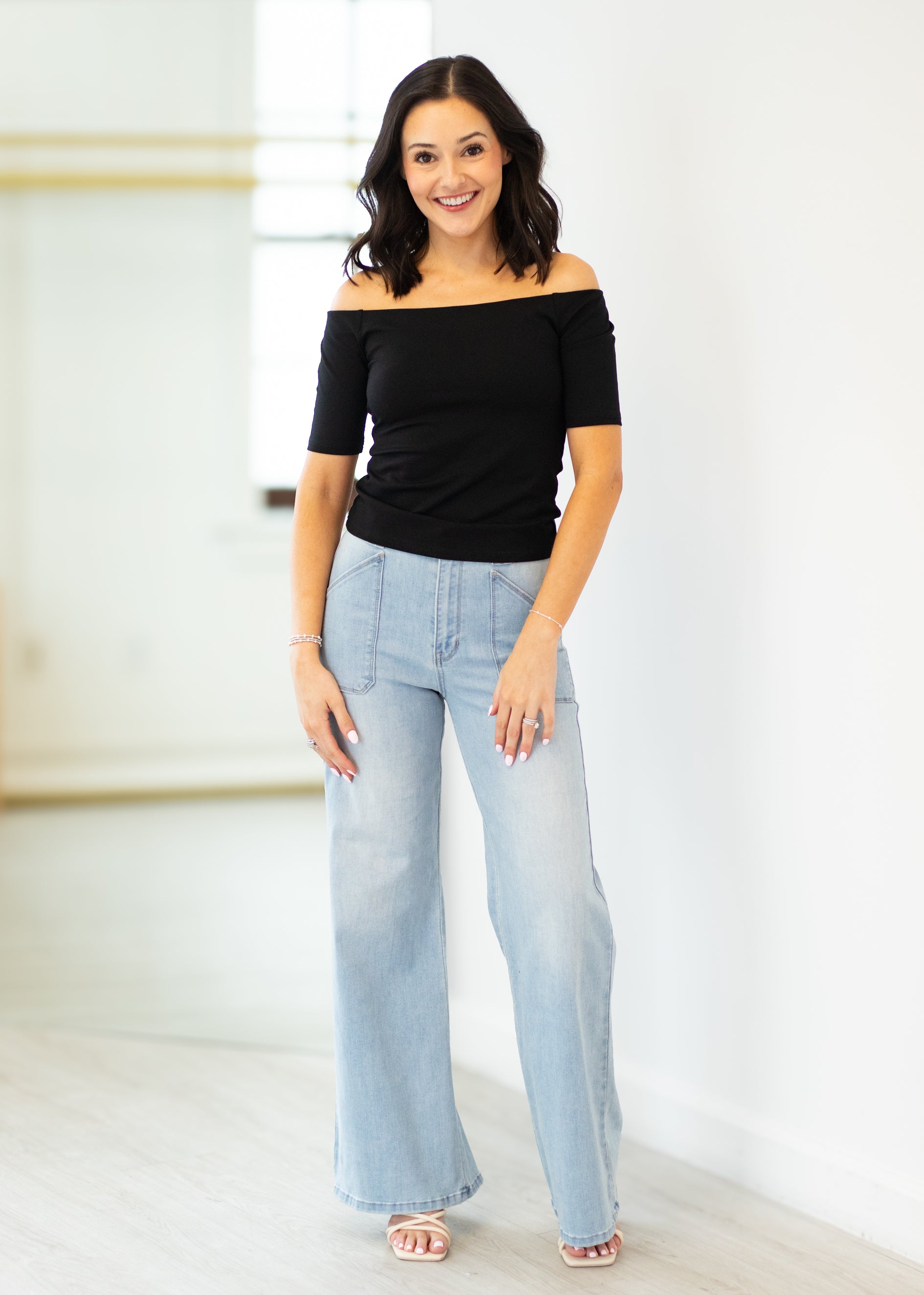 Woman wearing a black off-shoulder top and light blue jeans against a white background