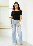 Woman wearing a black off-shoulder top and light blue jeans against a white background