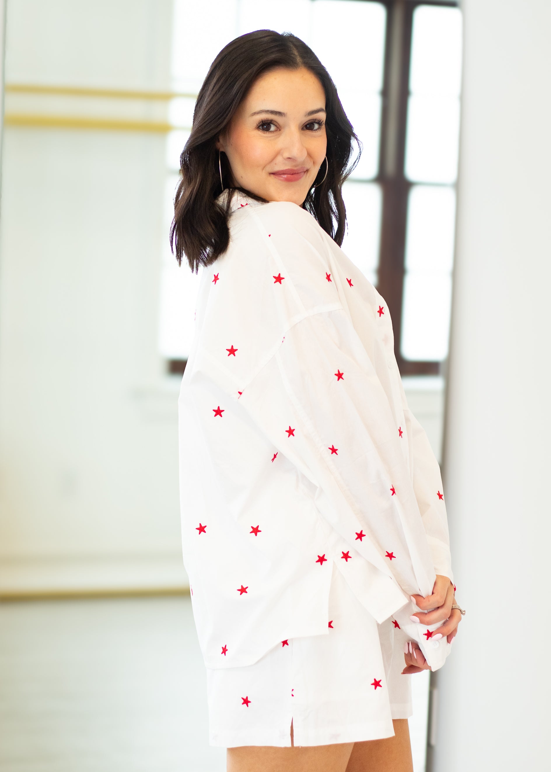 Woman wearing a white blouse with red star patterns indoors.