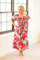Woman wearing a colorful floral dress in a bright room with large windows.