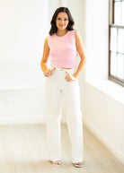 Woman wearing a pink sleeveless top and white pants in a bright room.