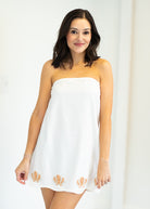 Woman wearing a white strapless dress with gold accents against a plain background