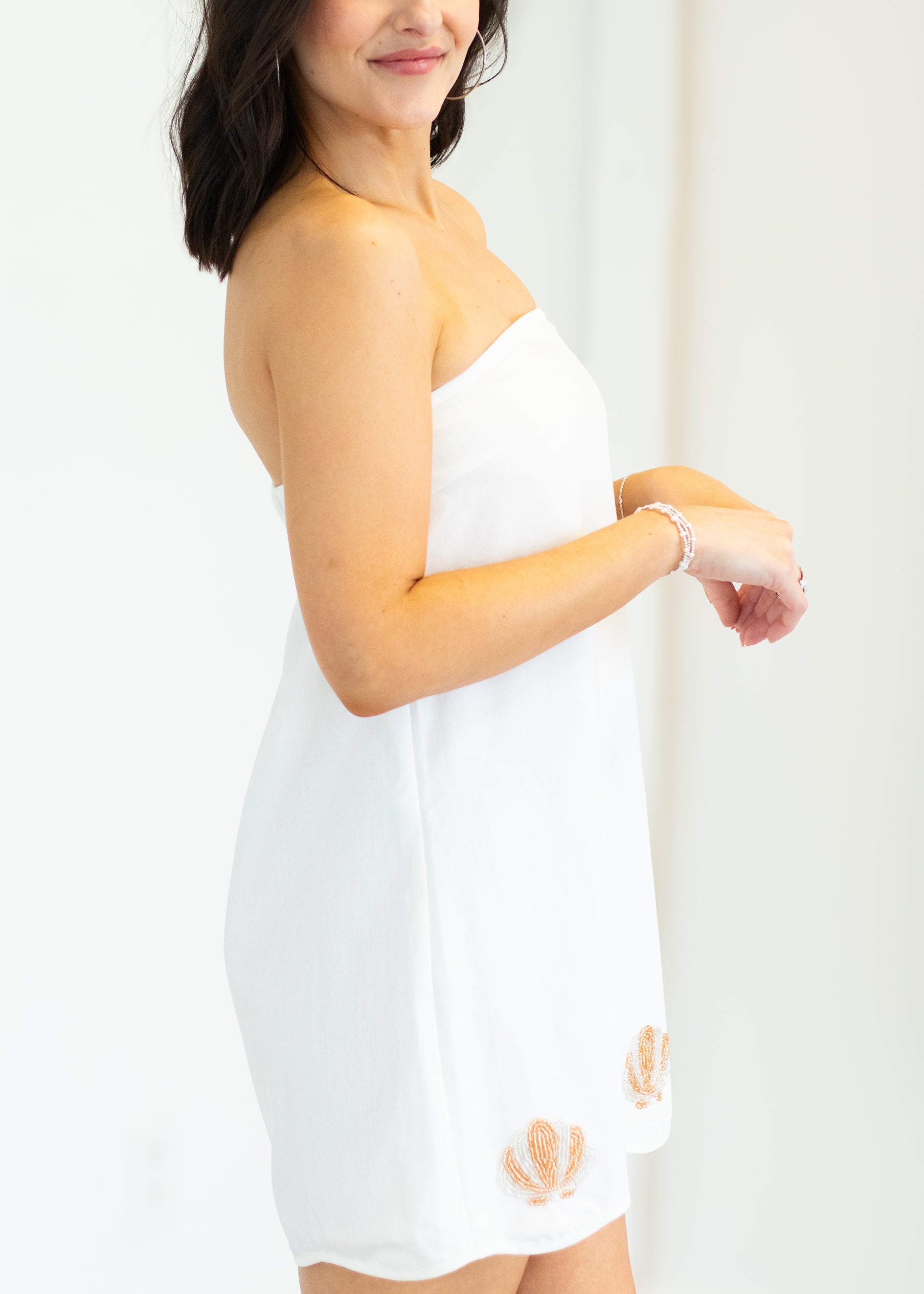 Woman wearing a white strapless dress with cut-out details on a plain background