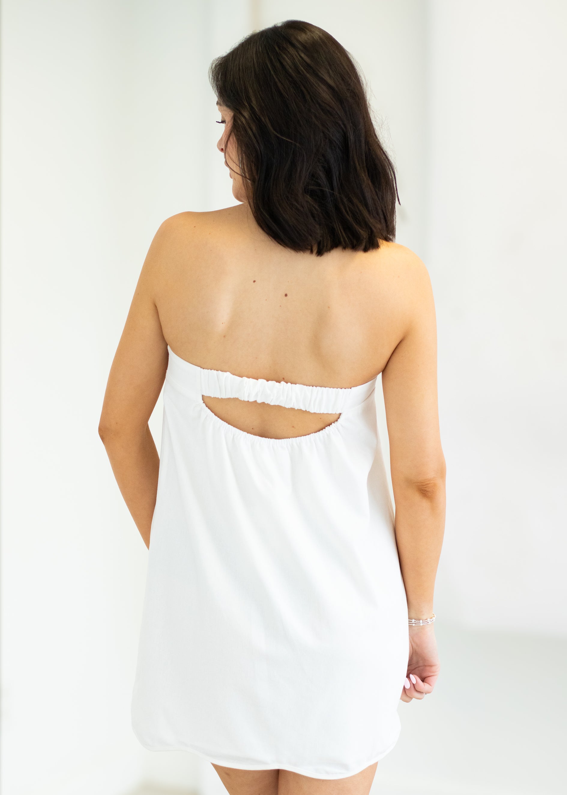 Woman wearing a white dress with cut-out back design on a plain background