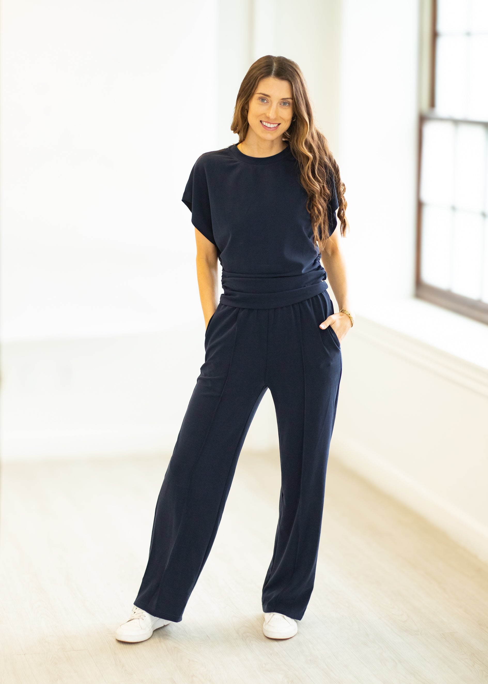 Woman wearing a navy outfit standing in a bright room.