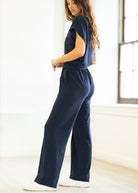 Woman wearing a navy blue jumpsuit in a bright room.
