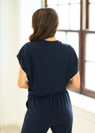 Woman wearing a navy blue outfit standing in a room with large windows.
