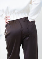 A close-up of a person wearing dark brown satin or silky wide-leg pants with a white side stripe, paired with a white ribbed sweater.