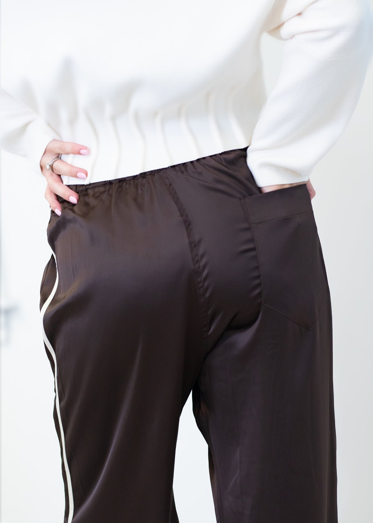 A close-up of a person wearing dark brown satin or silky wide-leg pants with a white side stripe, paired with a white ribbed sweater.