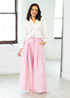 Woman wearing a white blouse and pink pants in a bright room.