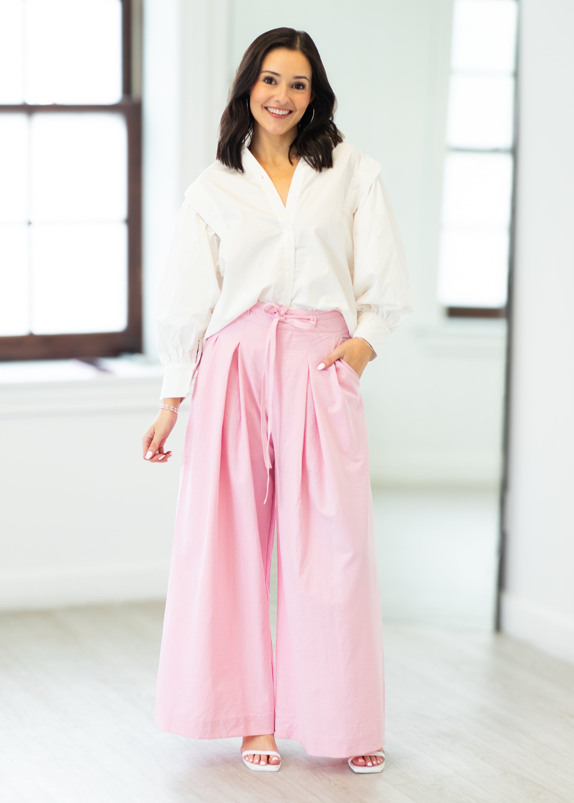 Woman wearing a white blouse and pink pants in a bright room.