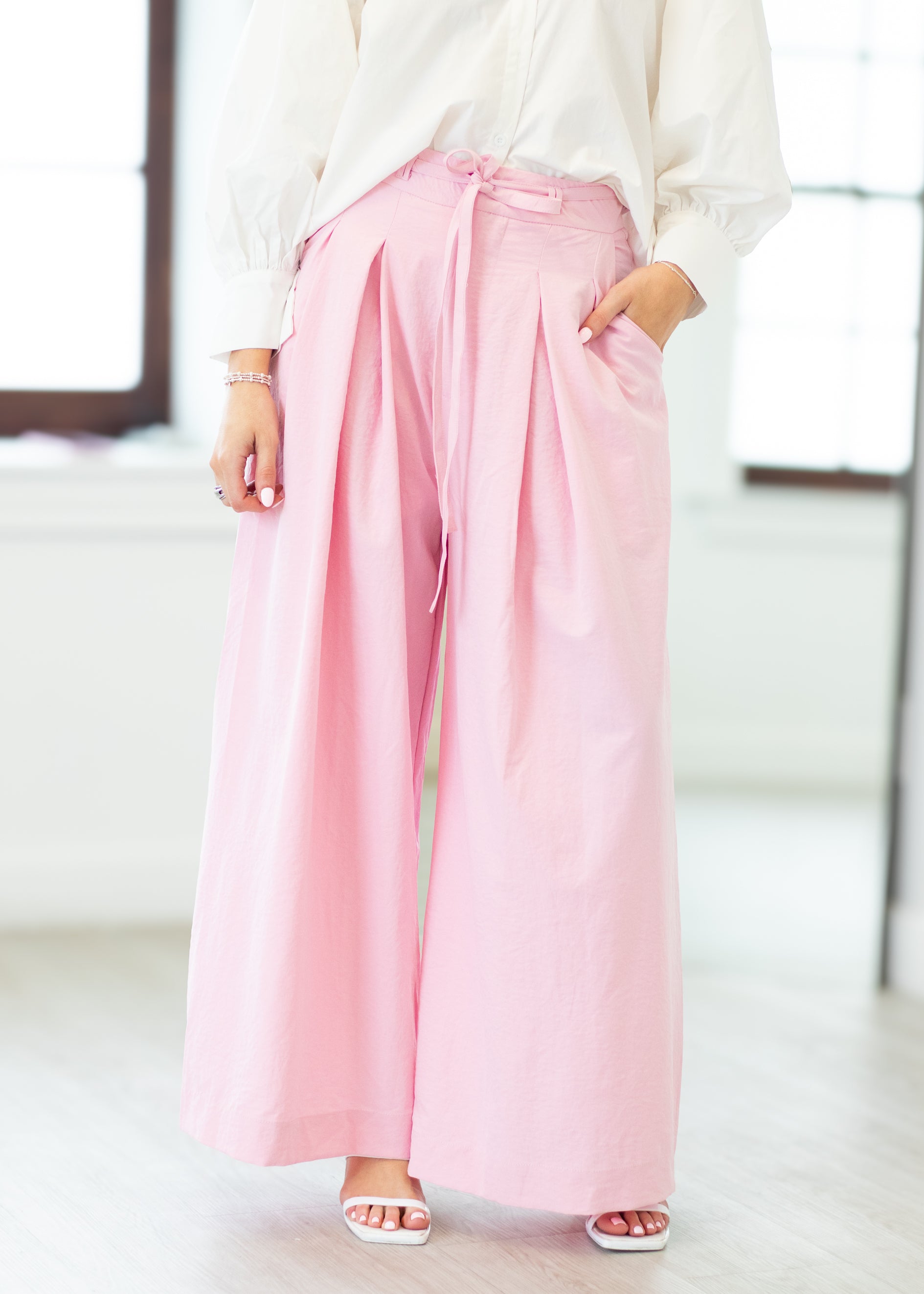 Person wearing light pink wide-leg pants with a blurred indoor background