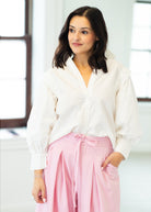 Woman wearing a white blouse and pink pants in a bright room.