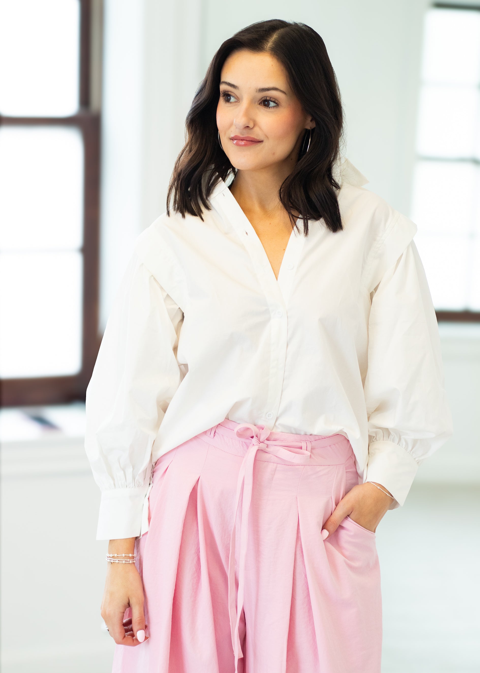 Woman wearing a white blouse and pink pants in a bright room.